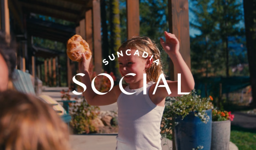 Smiling child in a white tank top holds a pastry outside on a sunny day, with the words Suncadia Social overlaid on the image.