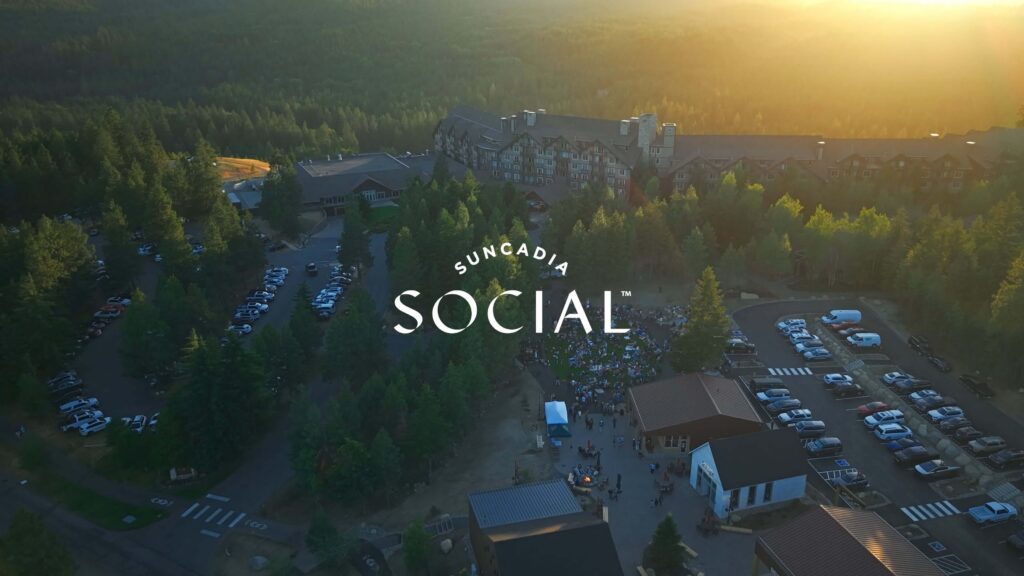 Aerial view of the Suncadia resort surrounded by forest at sunset, with parked cars and people gathering outside for Spring events at Suncadia, and the text Suncadia Social over the image.