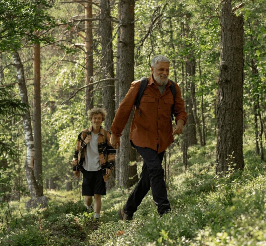 An older man with a beard and a young person walking together on a forest trail.